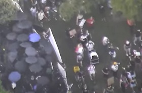 As riot squad assembles and prepare weapons under umbrellas at left - a weapons cart appears in the 'peaceful protest' mob at right As riot squad prepare weapons under umbrellas at left - a weapons cart is wheeled in by 'peaceful protest' mob at right